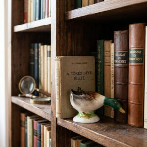 A hand-painted vintage Bodrogkeresztúri porcelain figurine of a wild duck hen with a lowered head, standing on a white lace doily over a yellow background. The figurine is in pristine condition.
