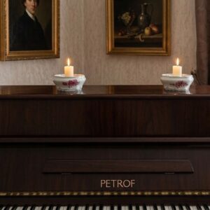 A pair of oval-shaped white vintage Czechoslovakian porcelain candle holders decorated with hand-painted pink flowers and silver scrollwork. Displayed with lit candles on top of a dark wood Petrof piano, creating a warm, elegant atmosphere.