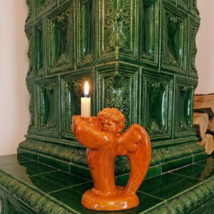 A vintage Art Deco style ceramic candlestick shaped like an angel with a vibrant orange glaze, holding a white candle, positioned on a dark green tiled stove.