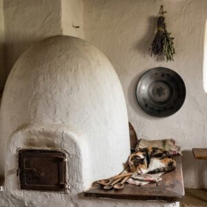 Interior lifestyle photo showing the black plate hanging on a white rustic wall next to a traditional clay oven and a sleeping calico cat.