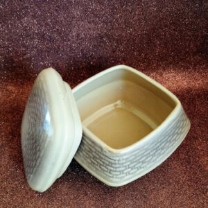 Open shot of the square ceramic bonbonnier base and the separate lid, interior visible, on a sparkly brown background.