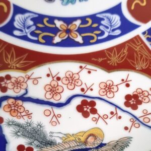 Close-up of the intricately painted chrysanthemum and plum blossom details in iron red, cobalt blue, and gold.